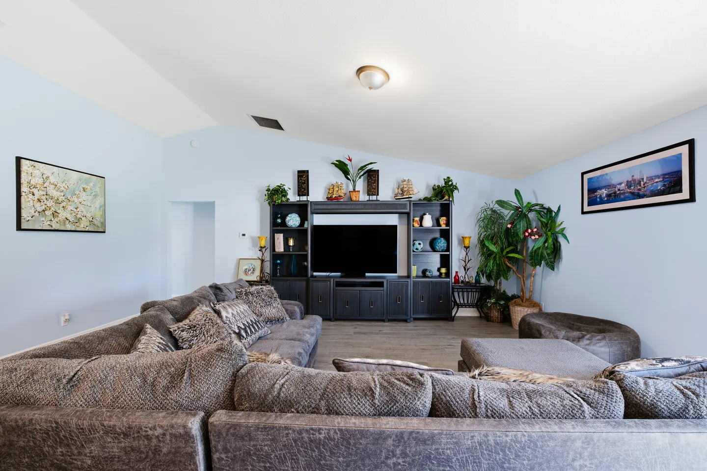 Living room with vaulted ceiling, large gray sectional couch, and dark entertainment center with a TV.