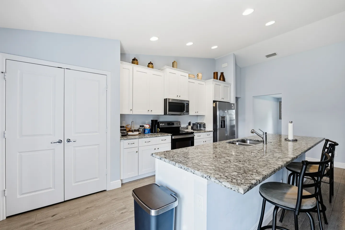 Kitchen with white shaker cabinets, speckled granite countertops, a large island with barstools, and stainless steel appliances.