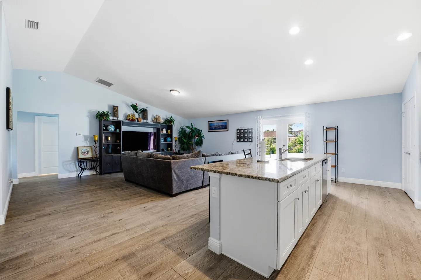 Open-concept living room and kitchen featuring vaulted ceilings, light wood-look flooring, and a kitchen island.