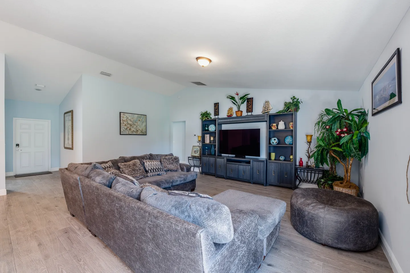 Living room with a large sectional sofa, round ottoman, and an entertainment center with a TV.