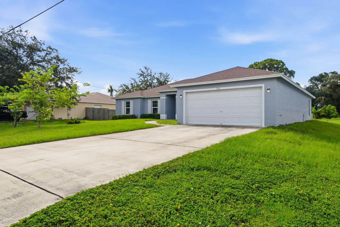 Exterior front view of a single-story light blue house with a wide concrete driveway and an attached two-car garage.