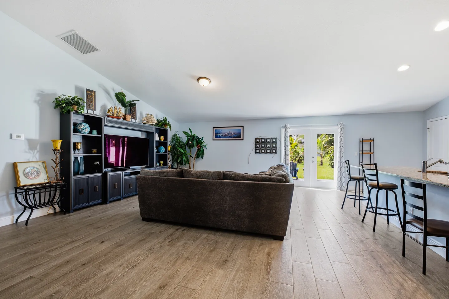 Open living area with wood-look plank flooring, a dark sectional sofa, a media center with TV, and French doors leading outside.