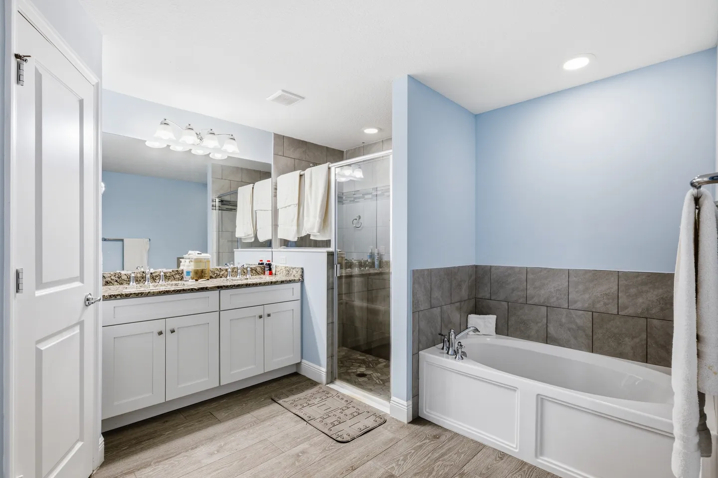 Bathroom with a double-sink vanity, glass-door walk-in shower, and a built-in soaking tub under light blue walls.