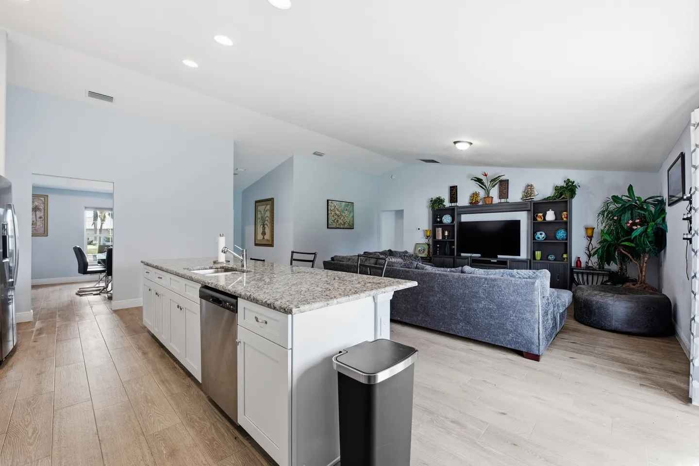 Open-concept living room and kitchen island with white cabinets, speckled countertops, and wood-look flooring.