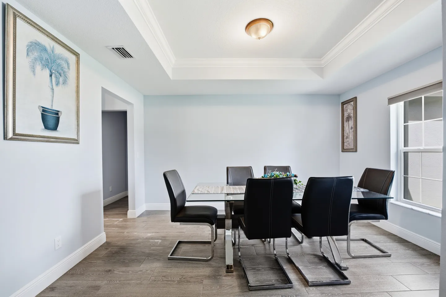 Dining room with a glass-topped table, modern black chairs, wood-look tile flooring, and a tray ceiling.