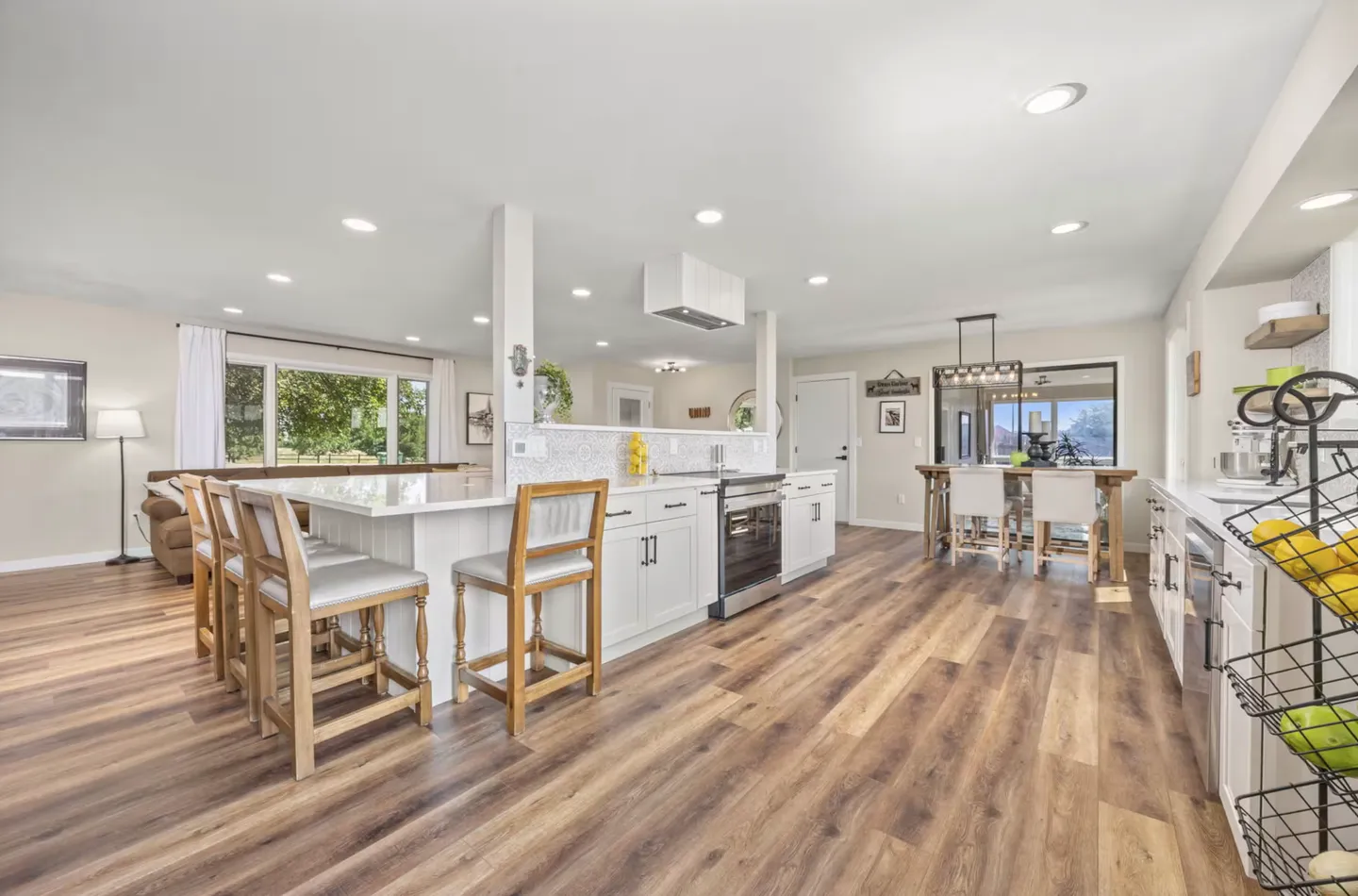 Open-concept interior showing kitchen island with bar stools, wood-style flooring, and adjacent dining area.