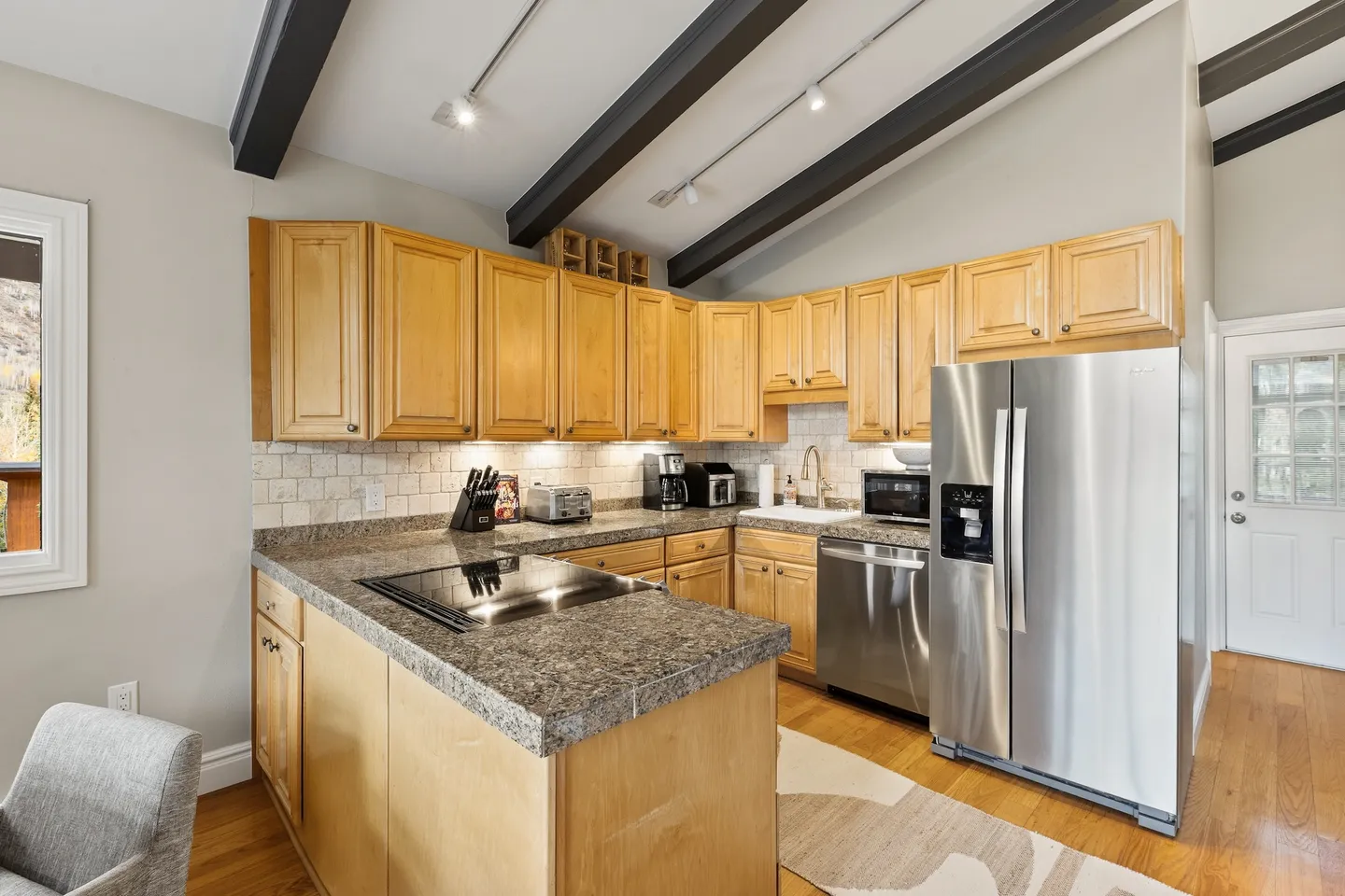 Kitchen with light wood cabinets, dark granite-look countertops, stainless steel appliances, and dark ceiling beams.