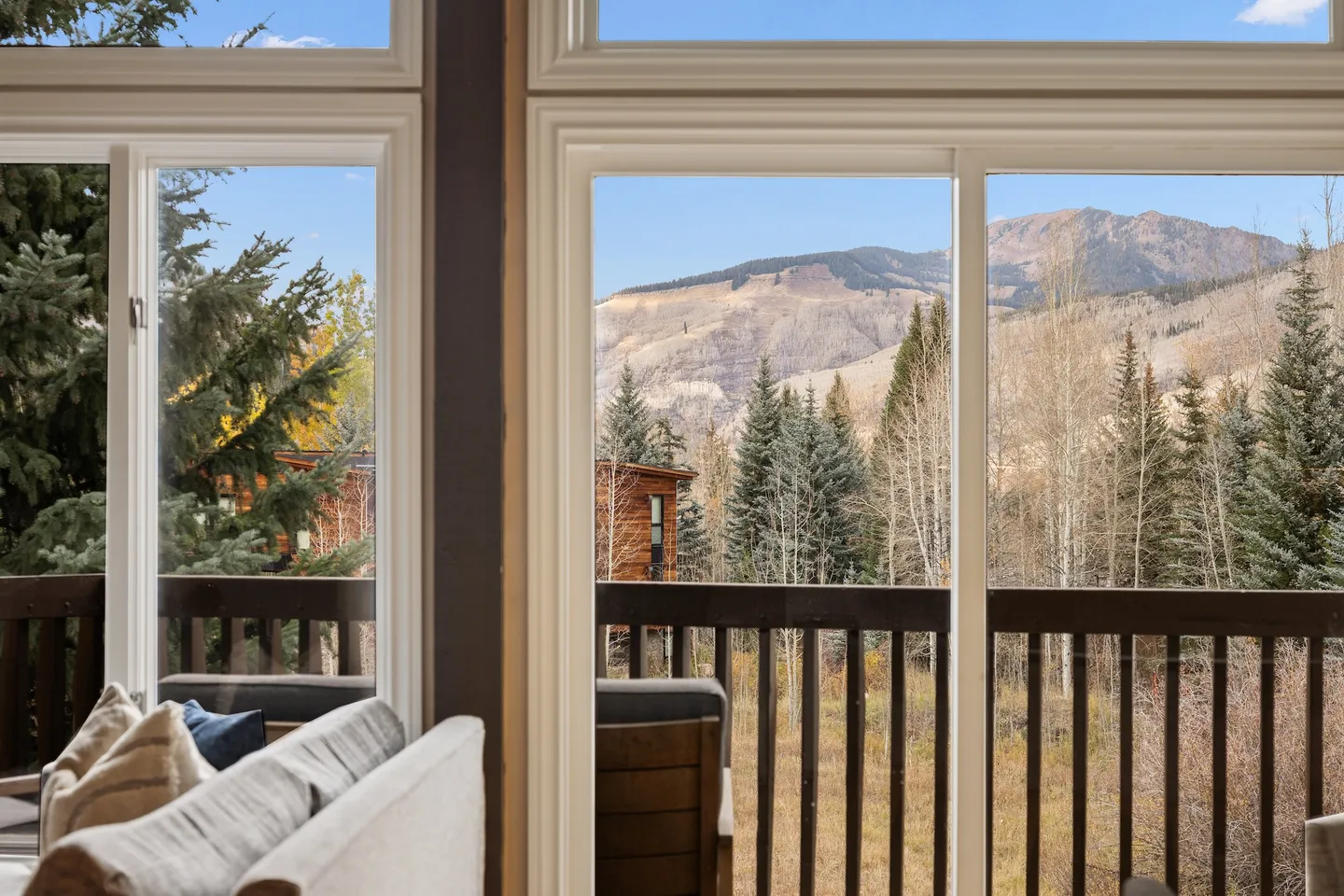 Large glass sliding doors framing a view of an outdoor deck, pine trees, and distant mountains under a blue sky.