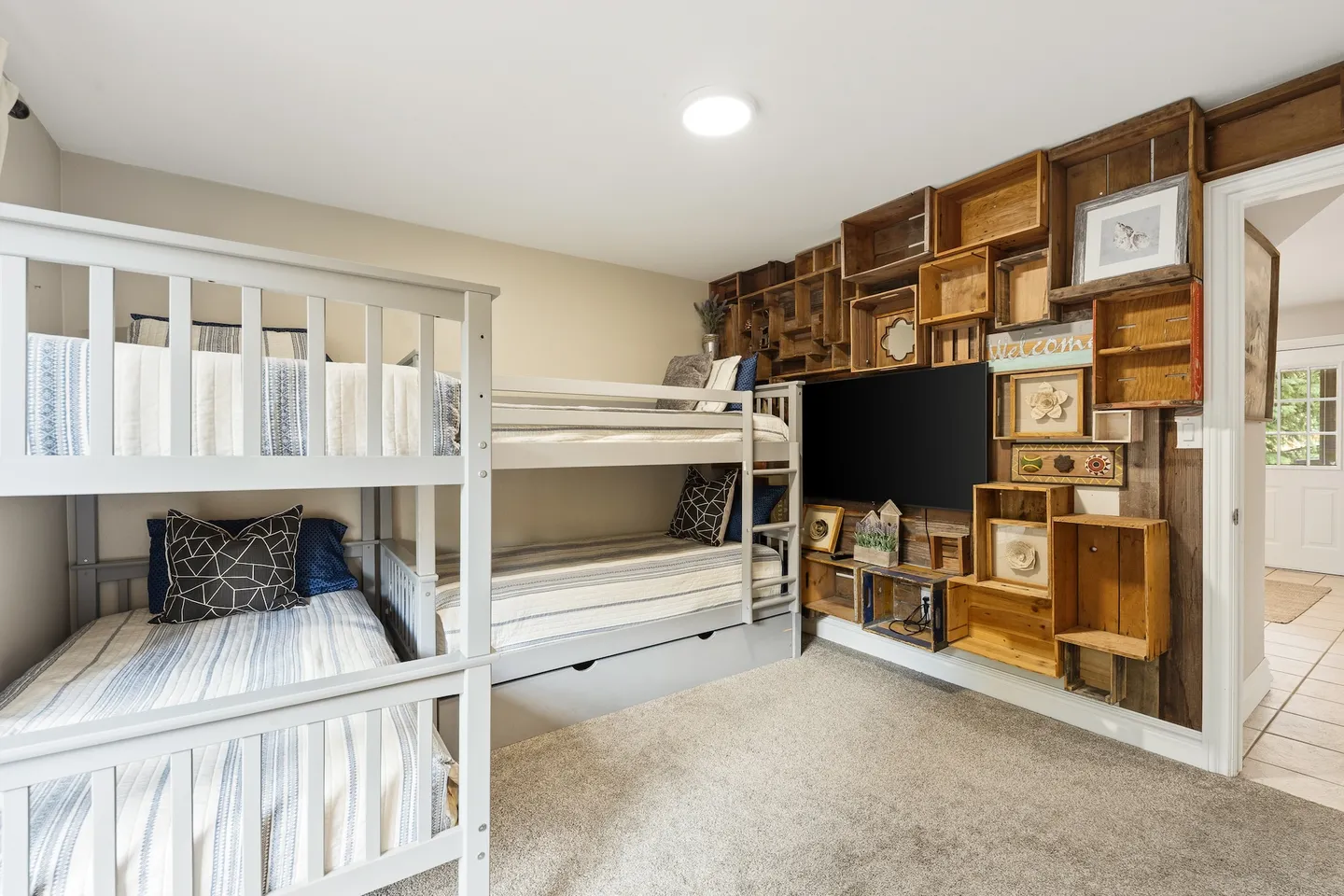 Bedroom featuring two sets of white wooden bunk beds and an accent wall crafted from wooden crates surrounding a flat-screen TV.