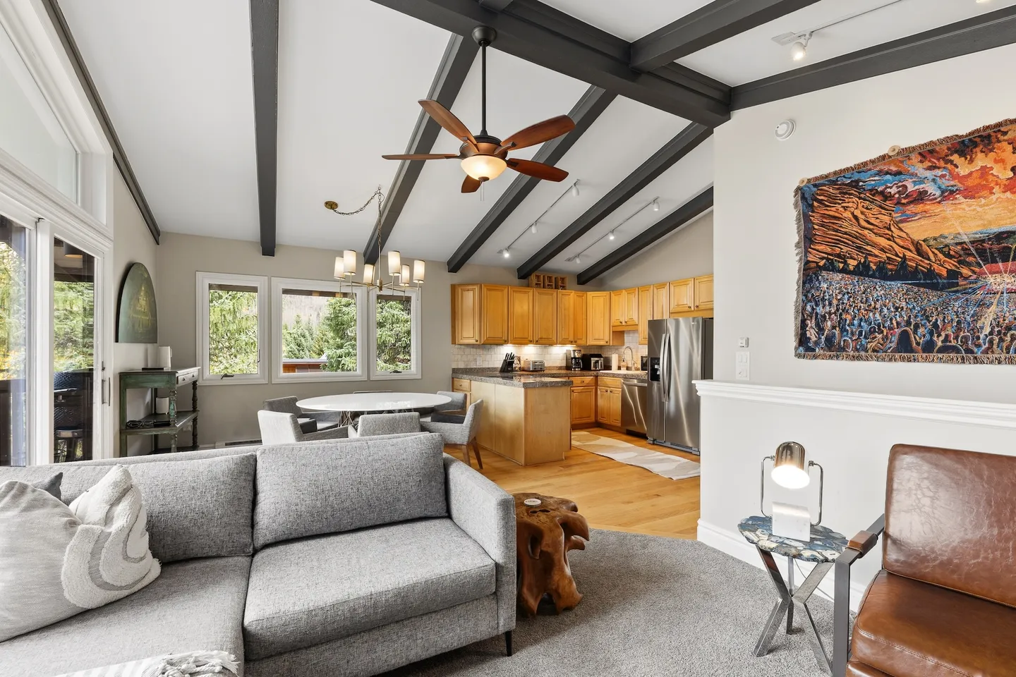 Open-concept living room, dining area, and kitchen with vaulted ceilings and exposed dark wood beams.