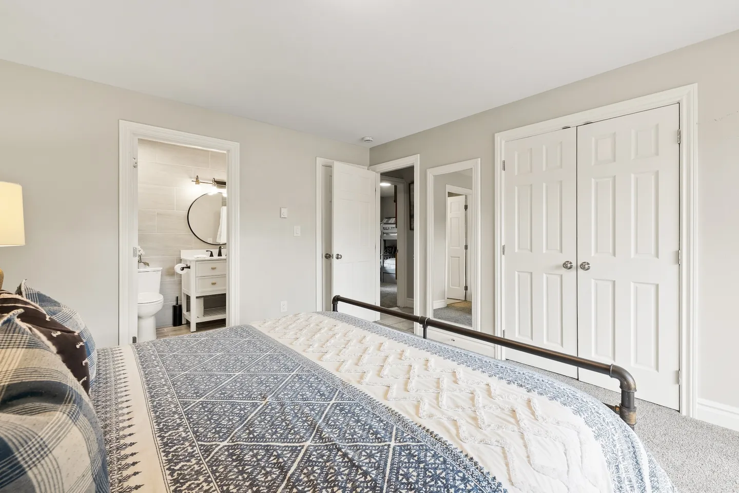 Bedroom with patterned bedding, an ensuite bathroom, a full-length mirror, and closet doors.