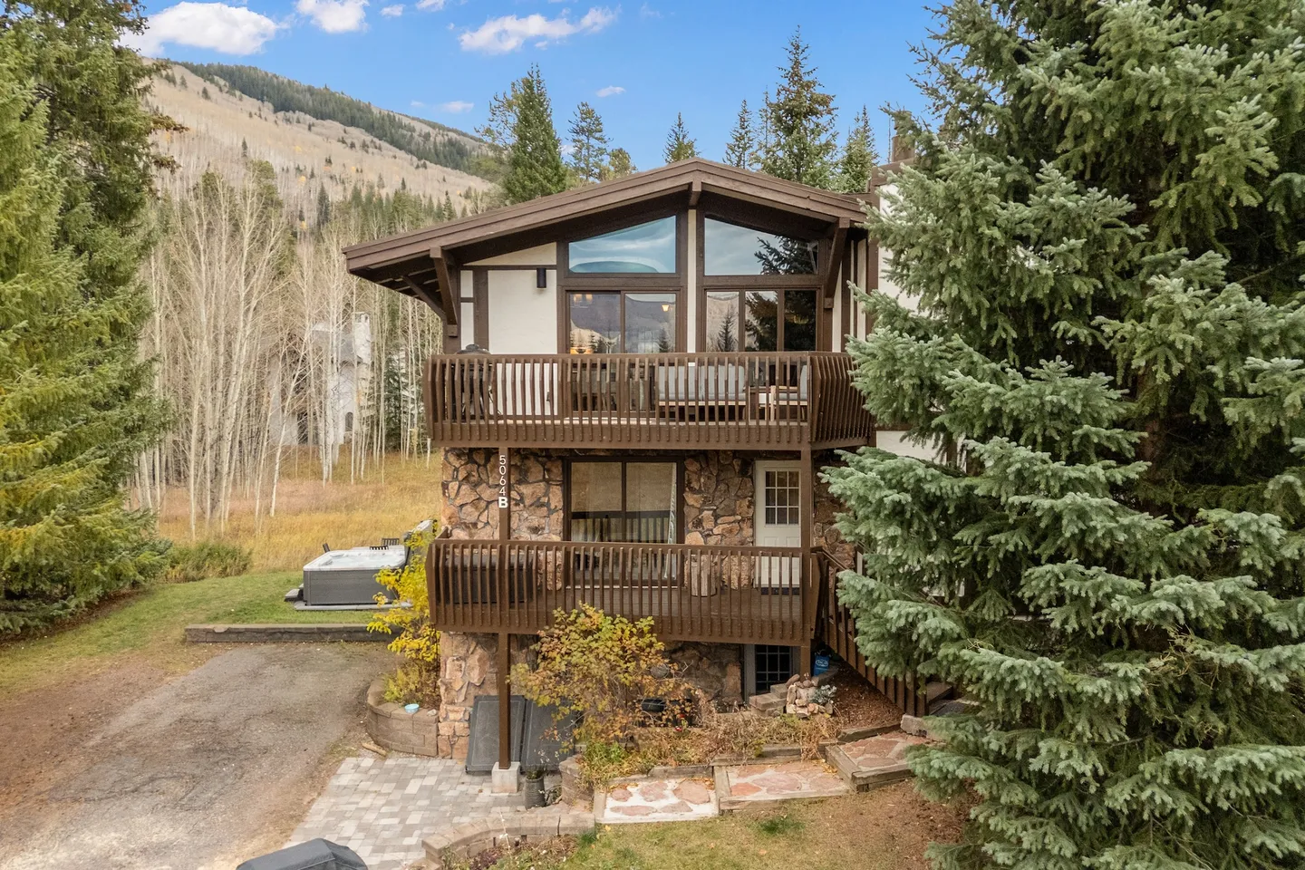 Exterior view of a multi-story mountain chalet with stone and wood siding, two wooden balconies, and evergreen trees.