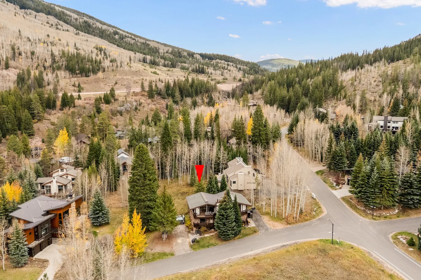 Aerial view of a mountain neighborhood surrounded by tall pine and aspen trees with a red marker pointing to a multi-story home.
