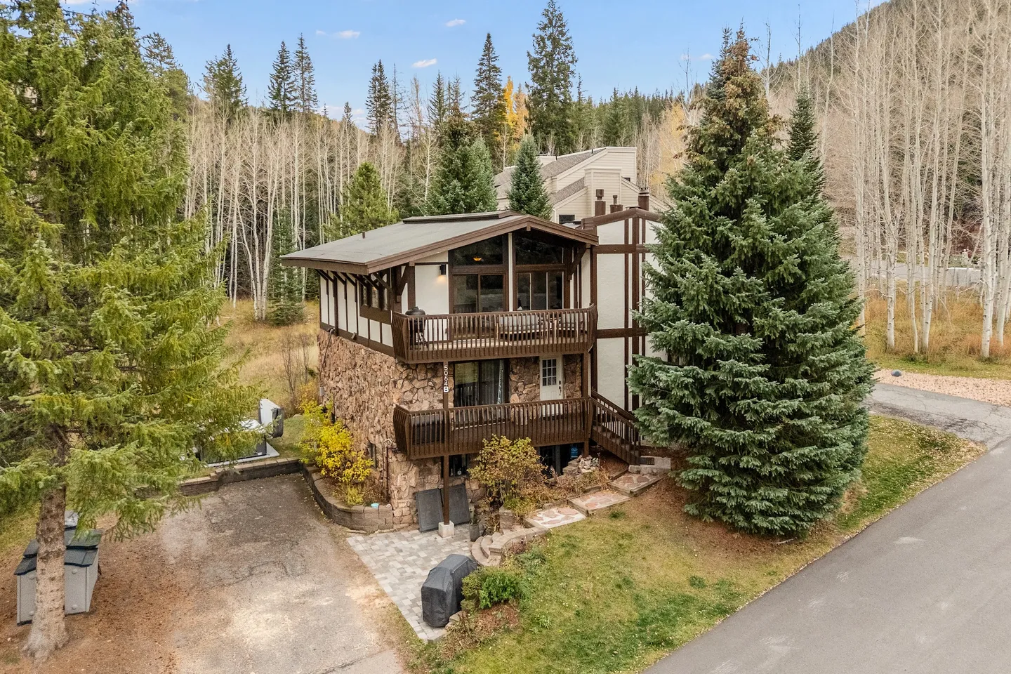Exterior view of a multi-story cabin-style home with stone siding, wooden balconies, and evergreen trees.