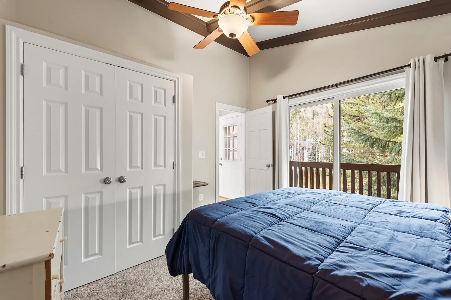 Bedroom with a bed made with a blue comforter, double closet doors, a ceiling fan, and sliding glass doors leading to a balcony.