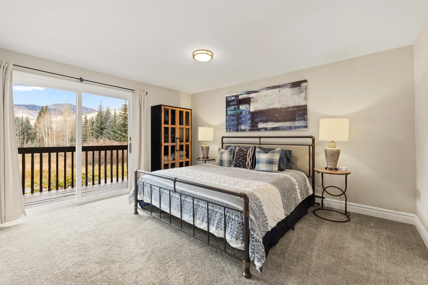 Bedroom with a metal-frame bed, bedside tables, and sliding glass doors opening to a balcony with mountain views.
