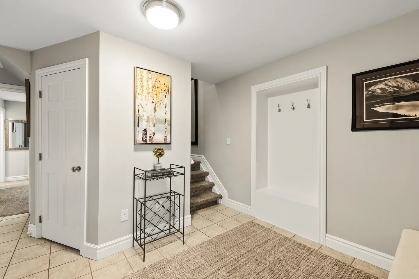 Entryway with tile flooring, a recessed coat rack bench, a small metal shelf, and carpeted stairs leading up.