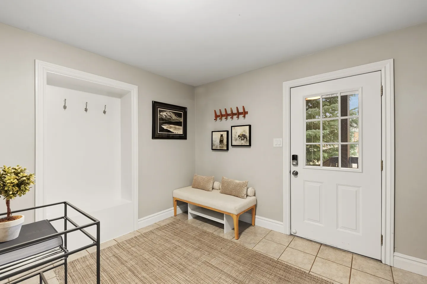 Entryway with a white front door featuring glass panes, a cushioned bench, wall hooks, framed artwork, and a built-in recessed nook with coat hooks.