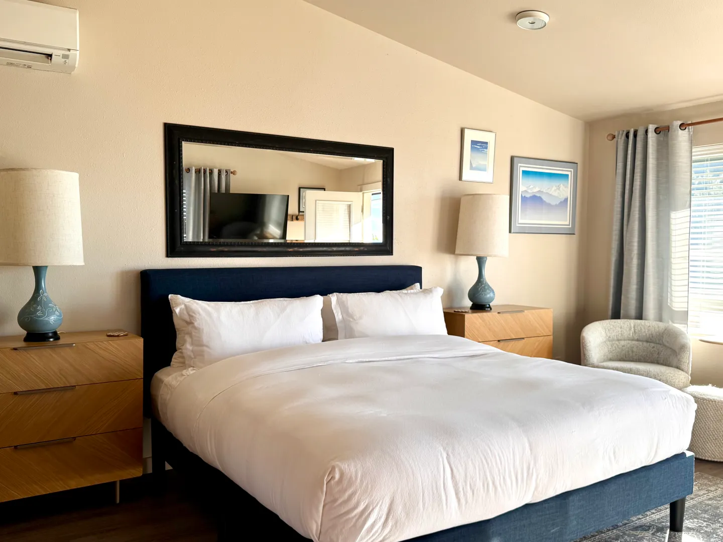 Bedroom with a navy upholstered bed, white bedding, wooden nightstands, matching lamps, and a large wall mirror.