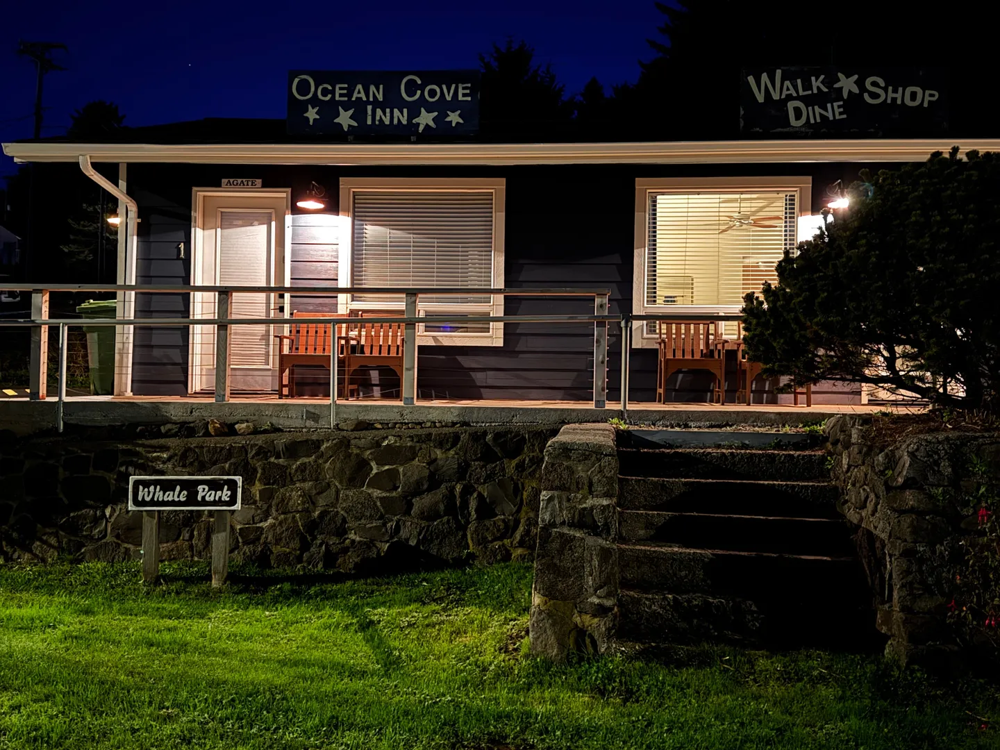 Night exterior view of Ocean Cove Inn with a porch, stone retaining wall, and front steps leading from the grass.