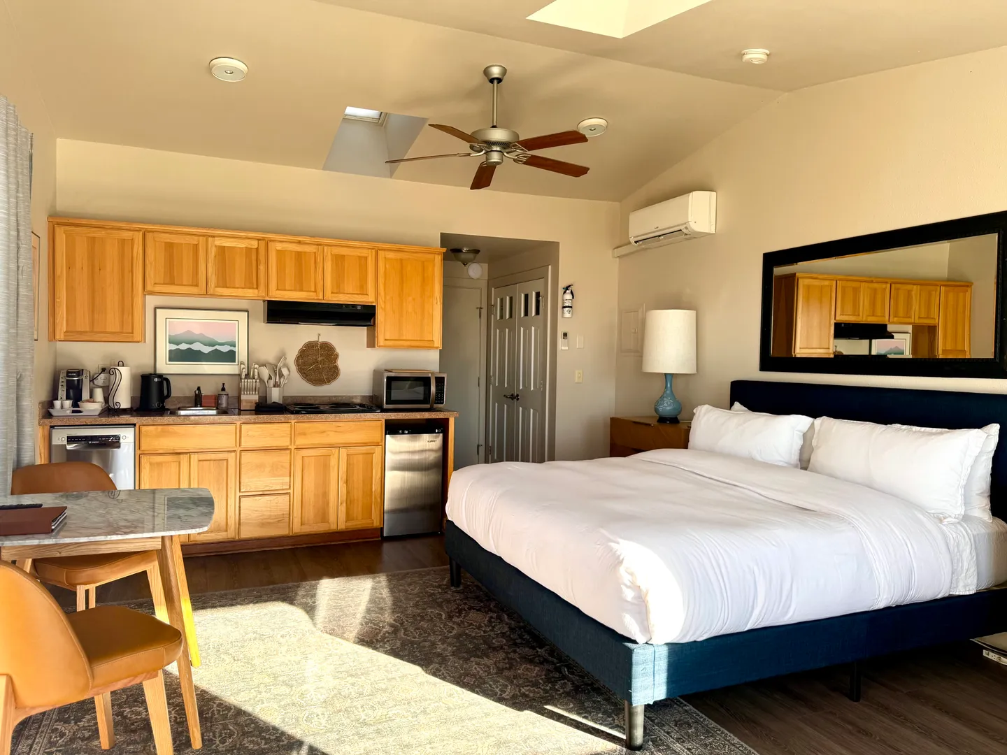 Studio living space featuring a bed with a dark blue frame, a compact kitchenette with wooden cabinets, and a small dining table.