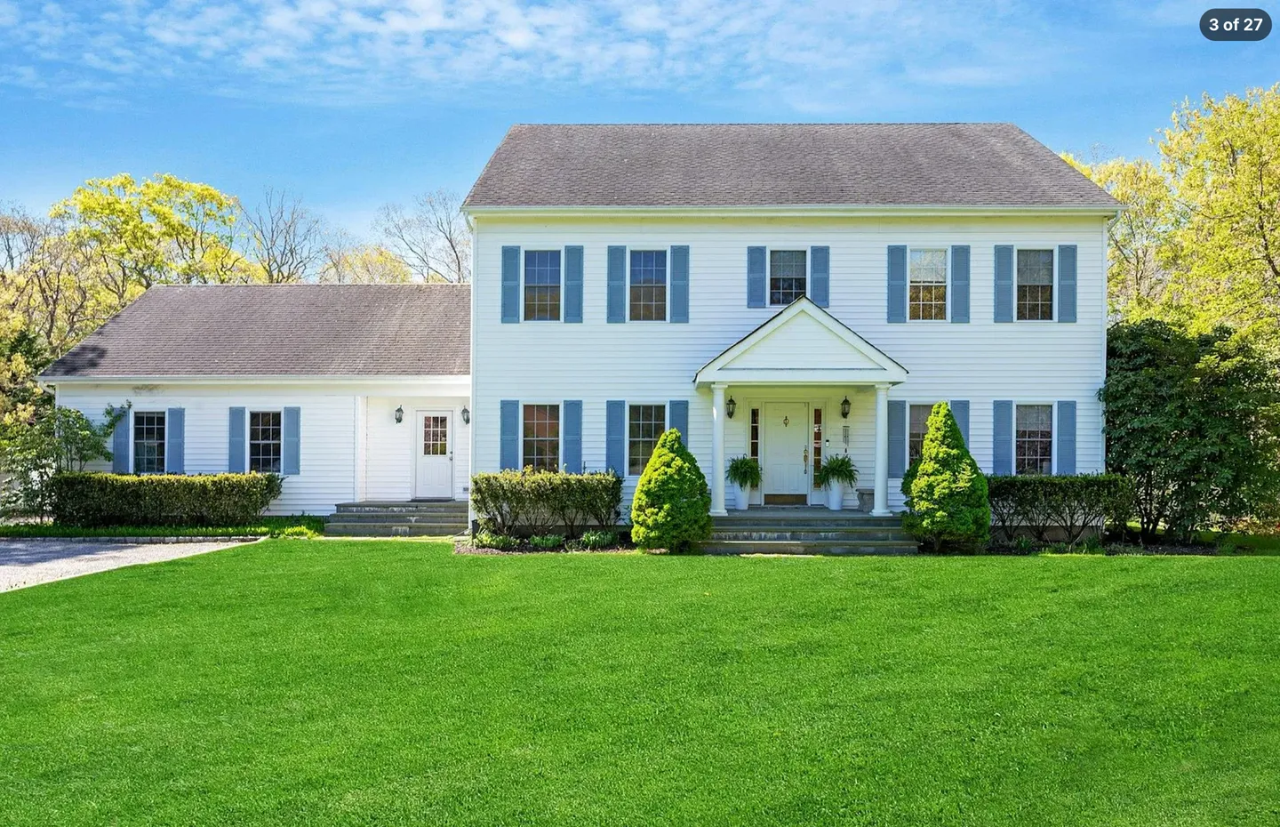 Front exterior of a two-story white house with blue shutters, a gabled portico entrance, and a green lawn.