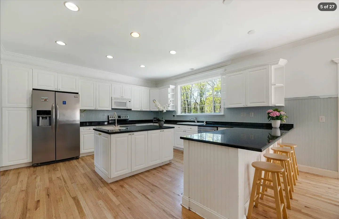 Spacious kitchen featuring white cabinetry, dark countertops, two islands, light wood flooring, and stainless steel refrigerator.