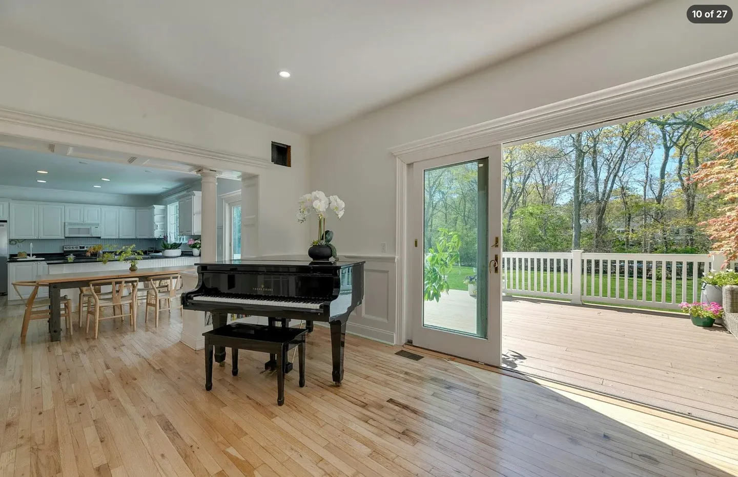 A black grand piano on light hardwood floors beside large sliding glass doors opening to a back deck.