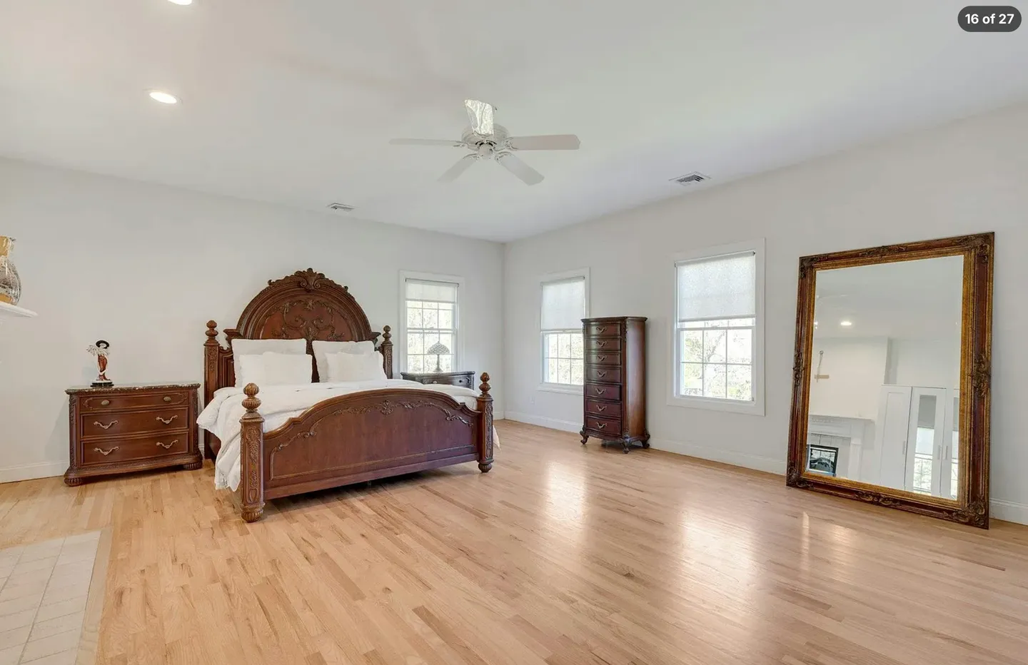 Spacious bedroom with light hardwood floors, a carved wooden bed frame, matching dressers, and a large leaning mirror.