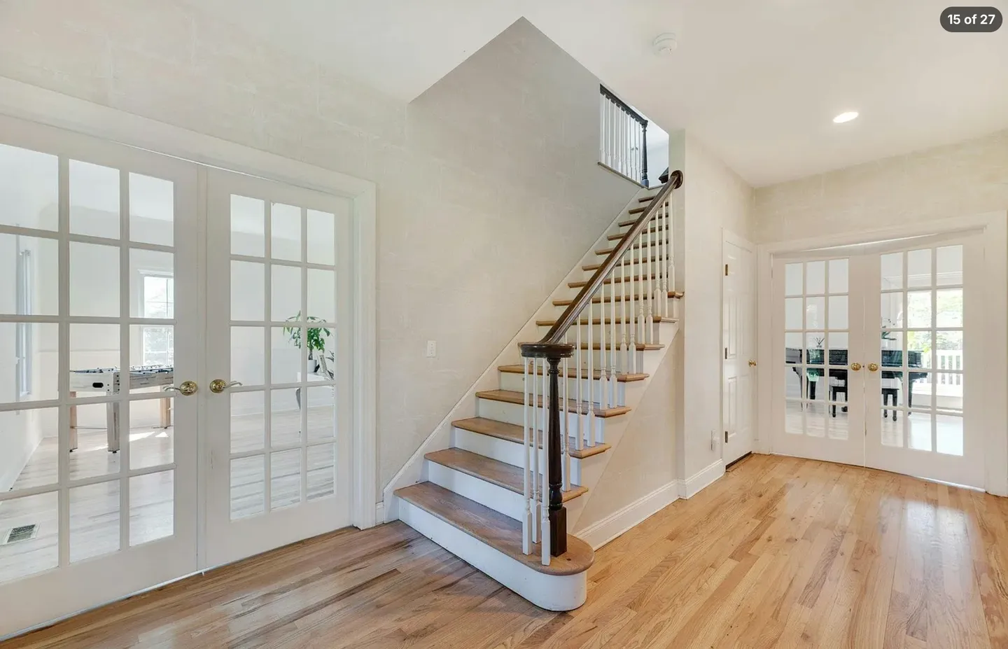 Entryway hallway with hardwood floors, a staircase with white spindles, and two sets of glass French doors leading to adjacent rooms.