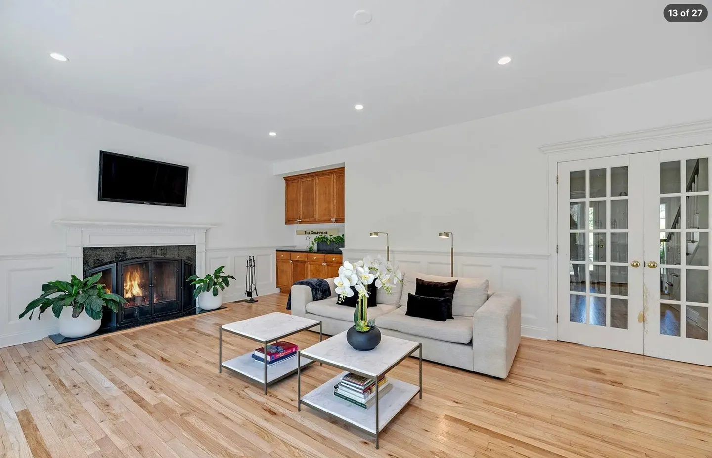 Living room featuring light hardwood floors, a lit fireplace, a sofa, two coffee tables, and glass double doors.