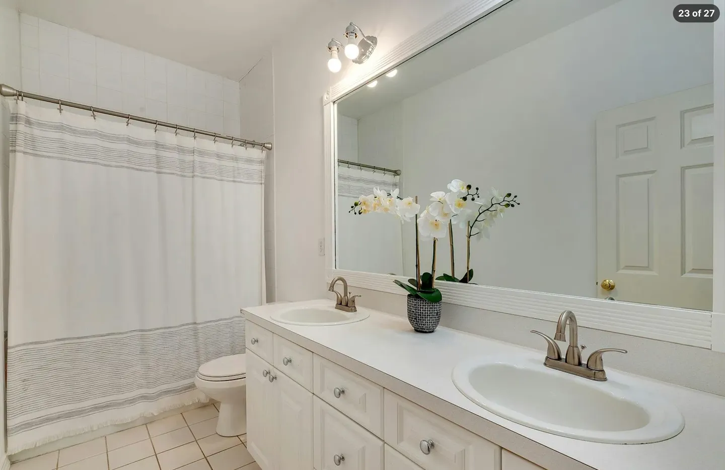 Bathroom featuring a double vanity with two sinks, a large framed mirror, and a shower curtain on the left.