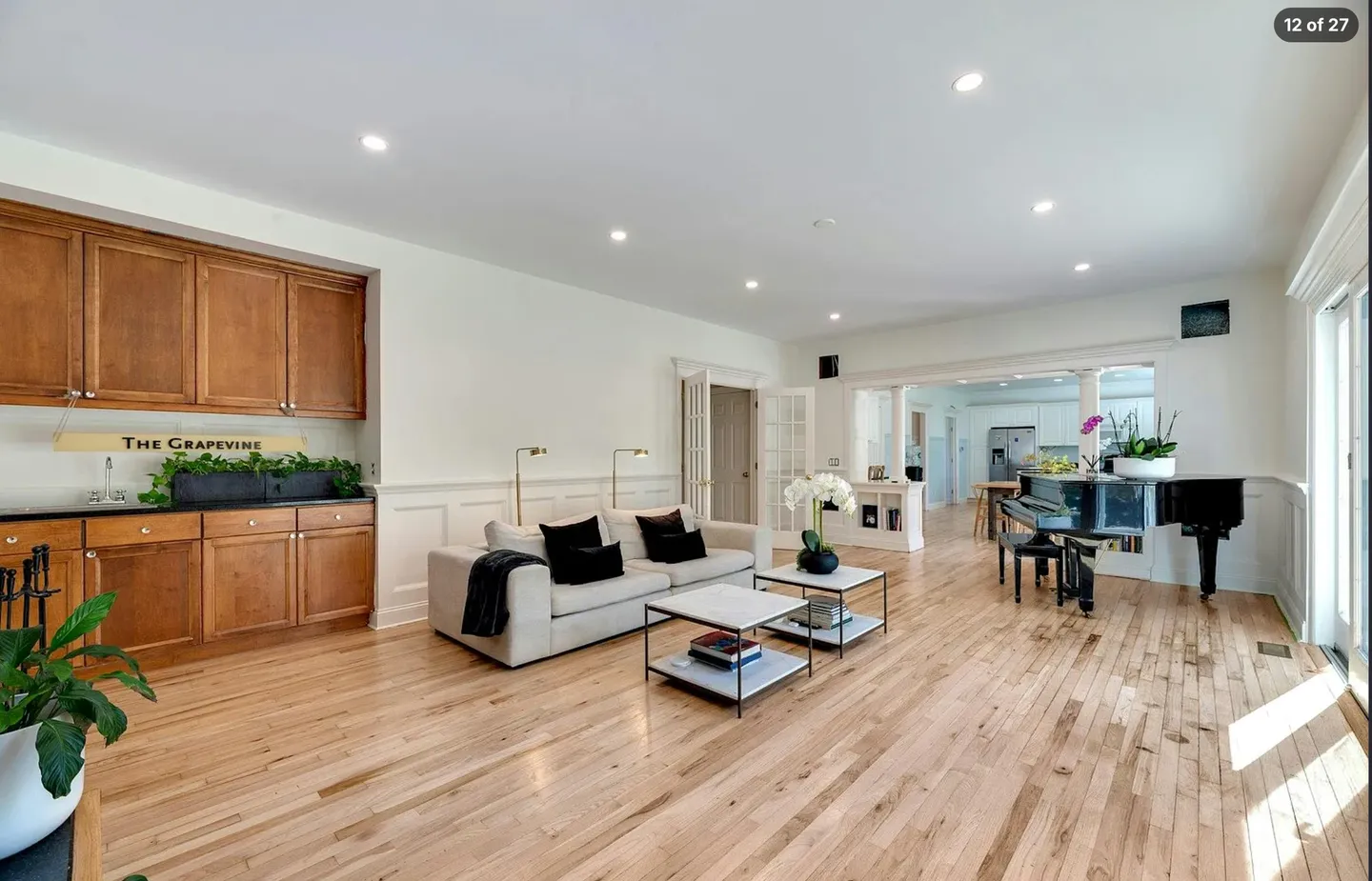 Spacious living room with light wood floors, a sofa, coffee tables, wet bar cabinetry, and a black grand piano.