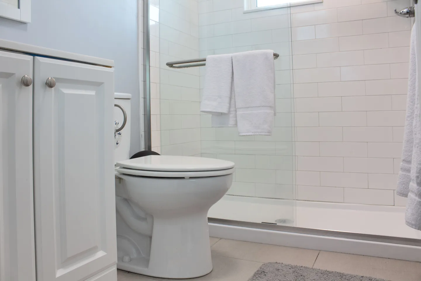Bathroom with white toilet next to a glass-enclosed walk-in shower lined with white subway tile.