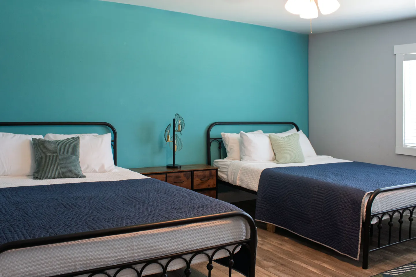 Bedroom featuring two black metal frame beds against a bright turquoise accent wall, with a small nightstand between them.