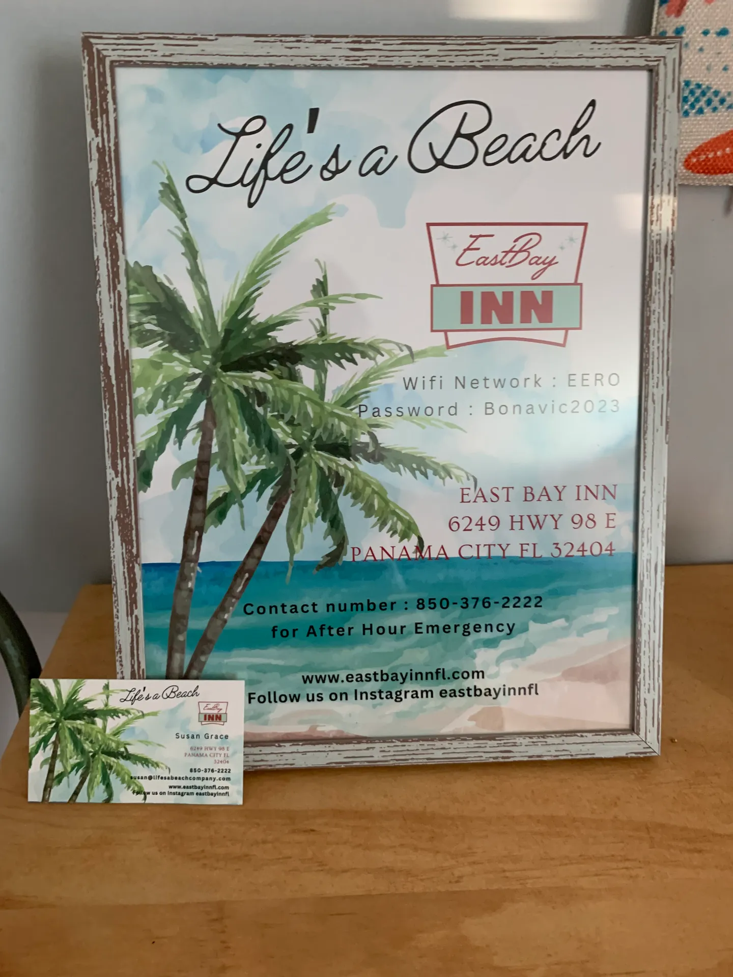 Framed guest information sign for East Bay Inn with Wi-Fi details and business card on a wooden surface.