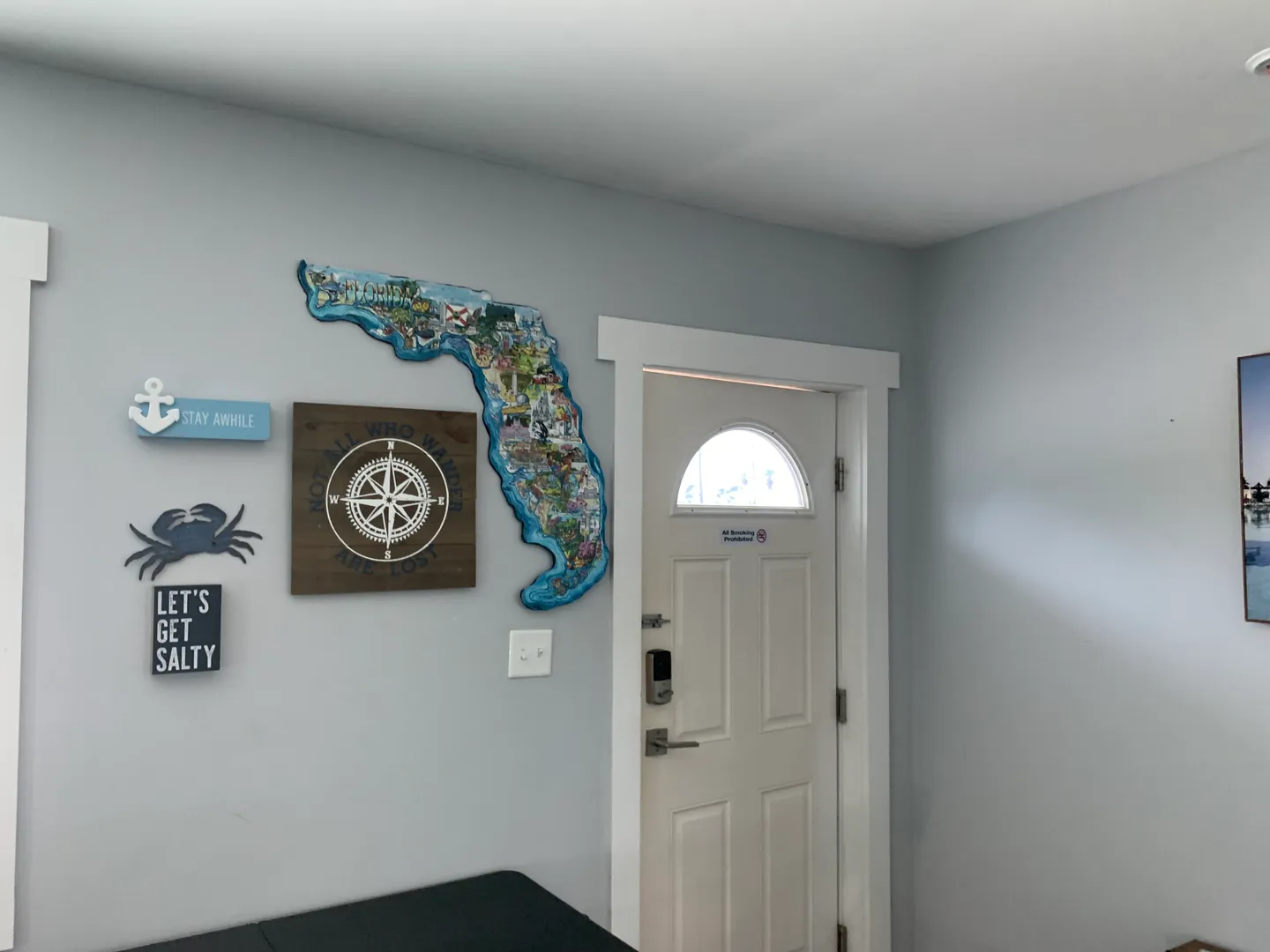 Entryway door with smart lock keypad next to light blue wall decorated with coastal signs and a Florida-shaped map.