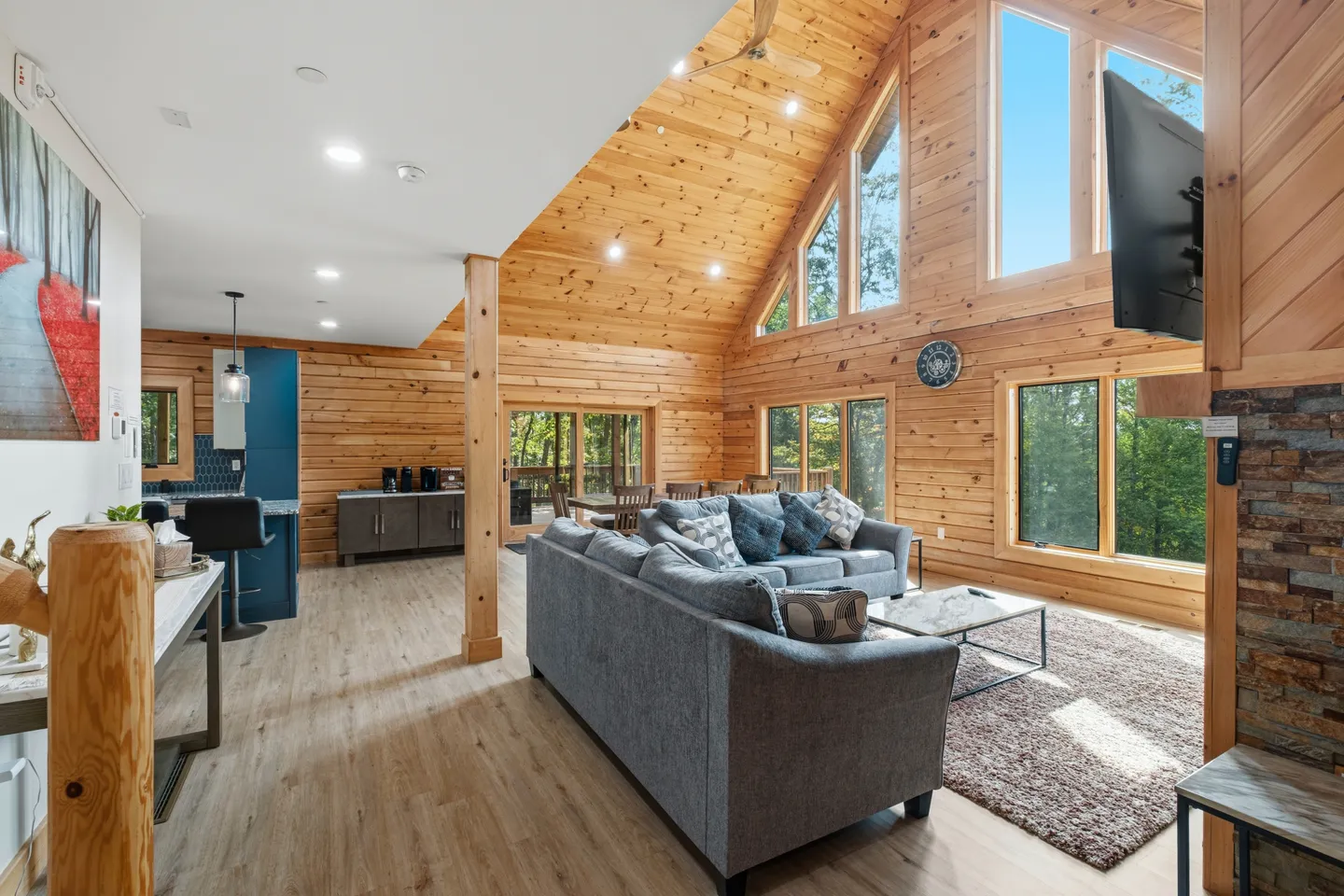 Open-concept living room and kitchen in a log-style cabin with vaulted pine ceilings and large A-frame windows.