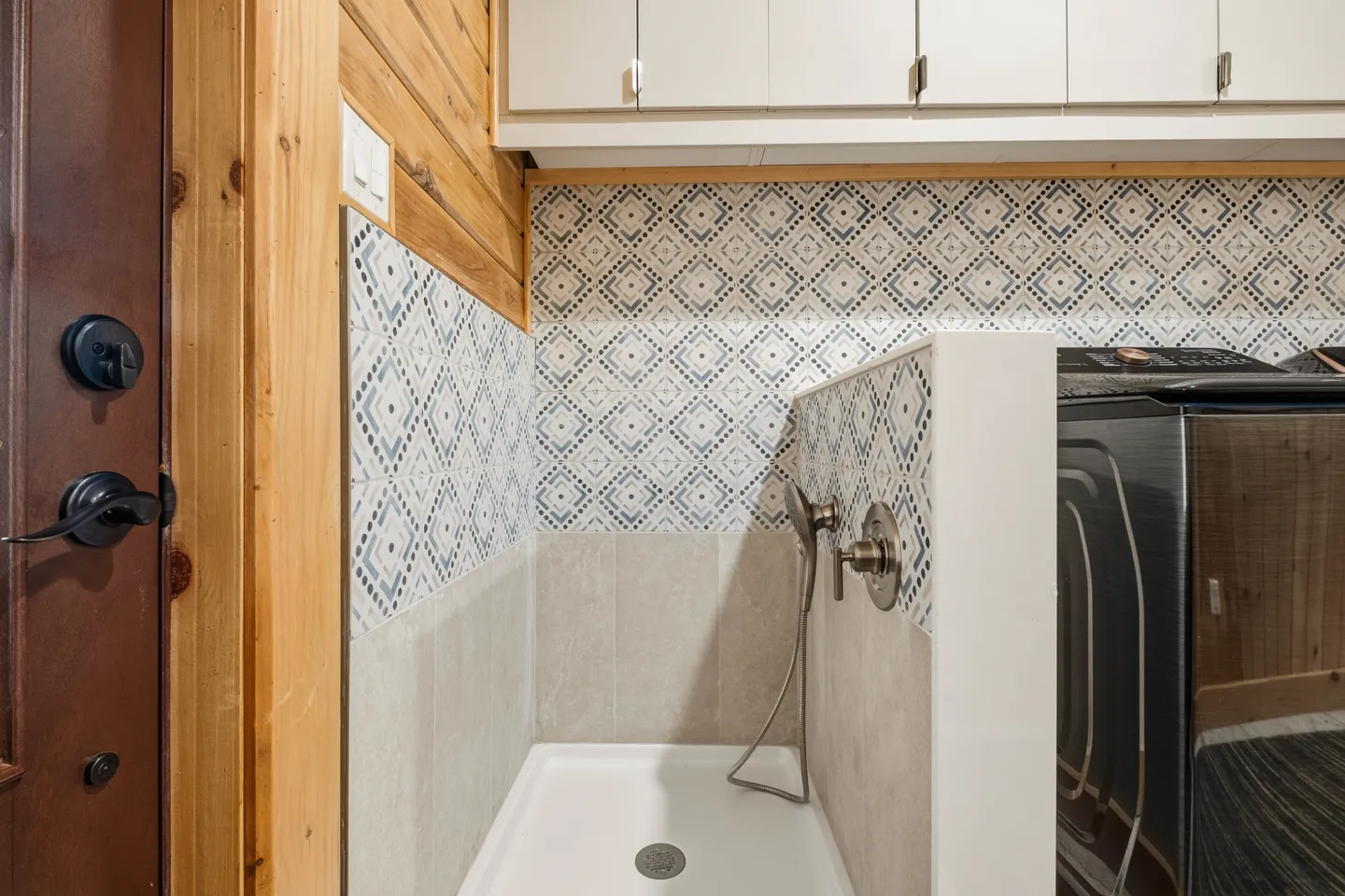 A dedicated pet washing station with patterned tile and a handheld sprayer, located beside laundry appliances.