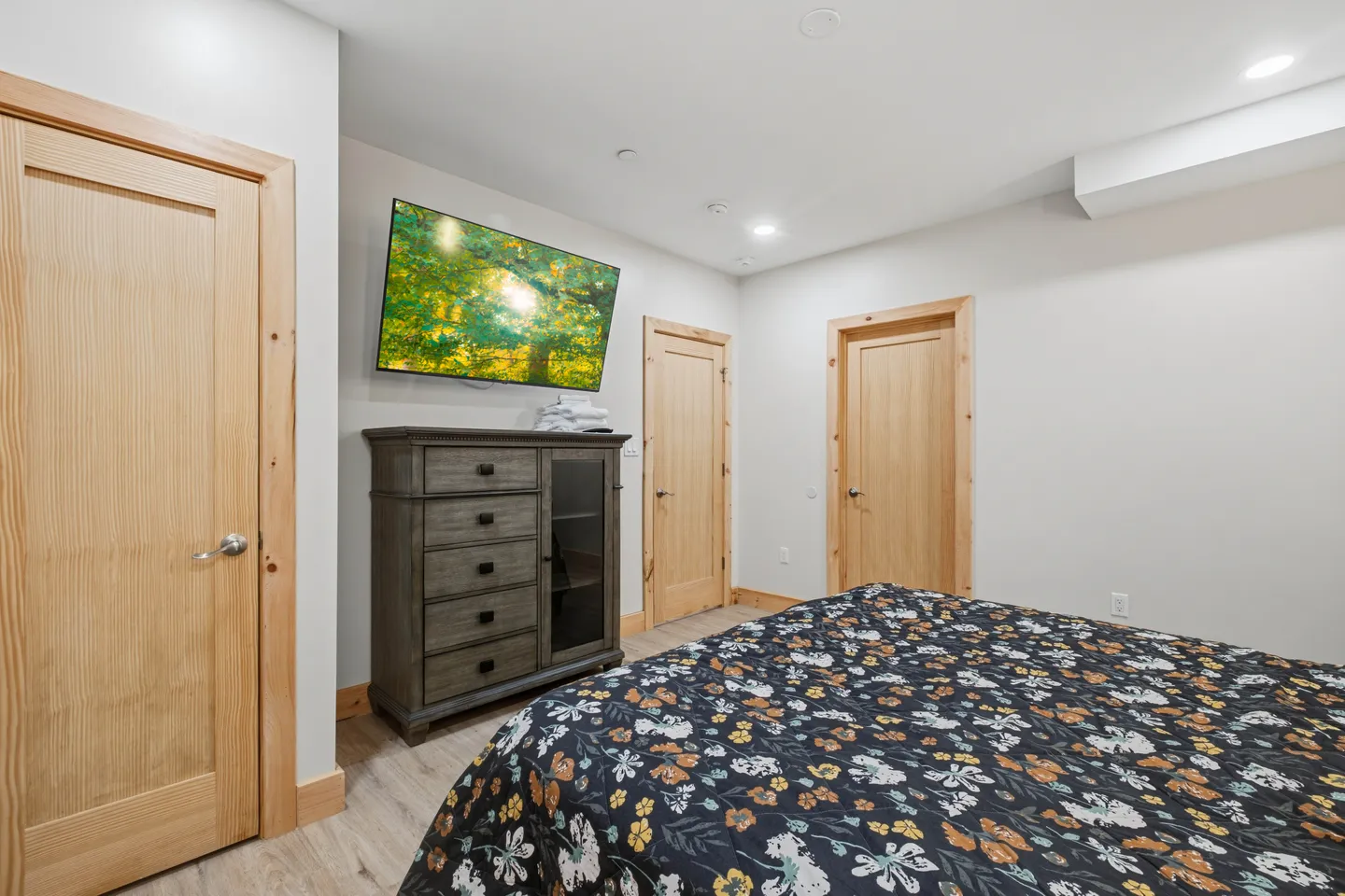 Bedroom featuring a floral patterned bedspread, wood dresser, wall-mounted television, and light wood interior doors.