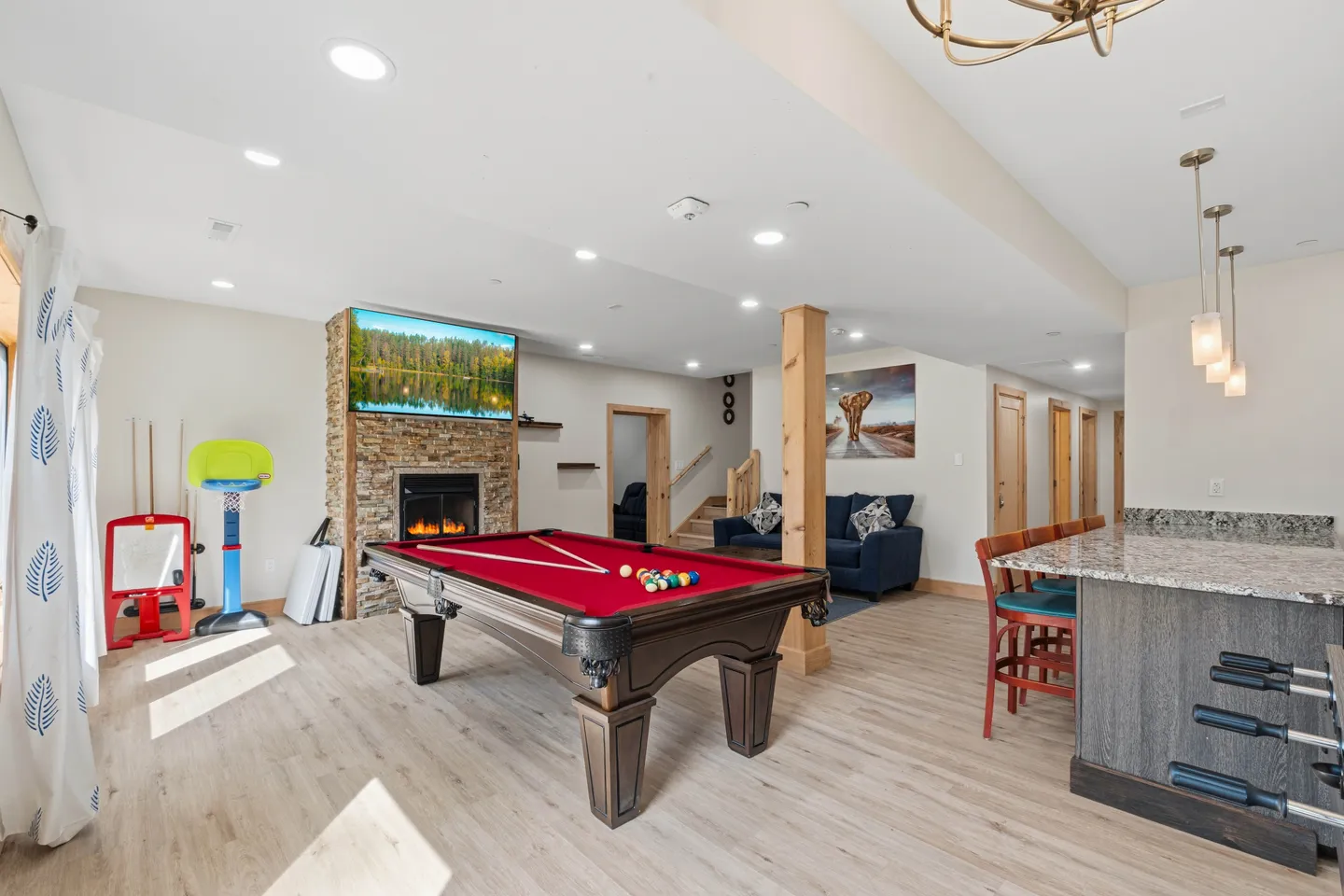Game room featuring a red-felt pool table, stone fireplace with a television above it, and a bar counter with seating.