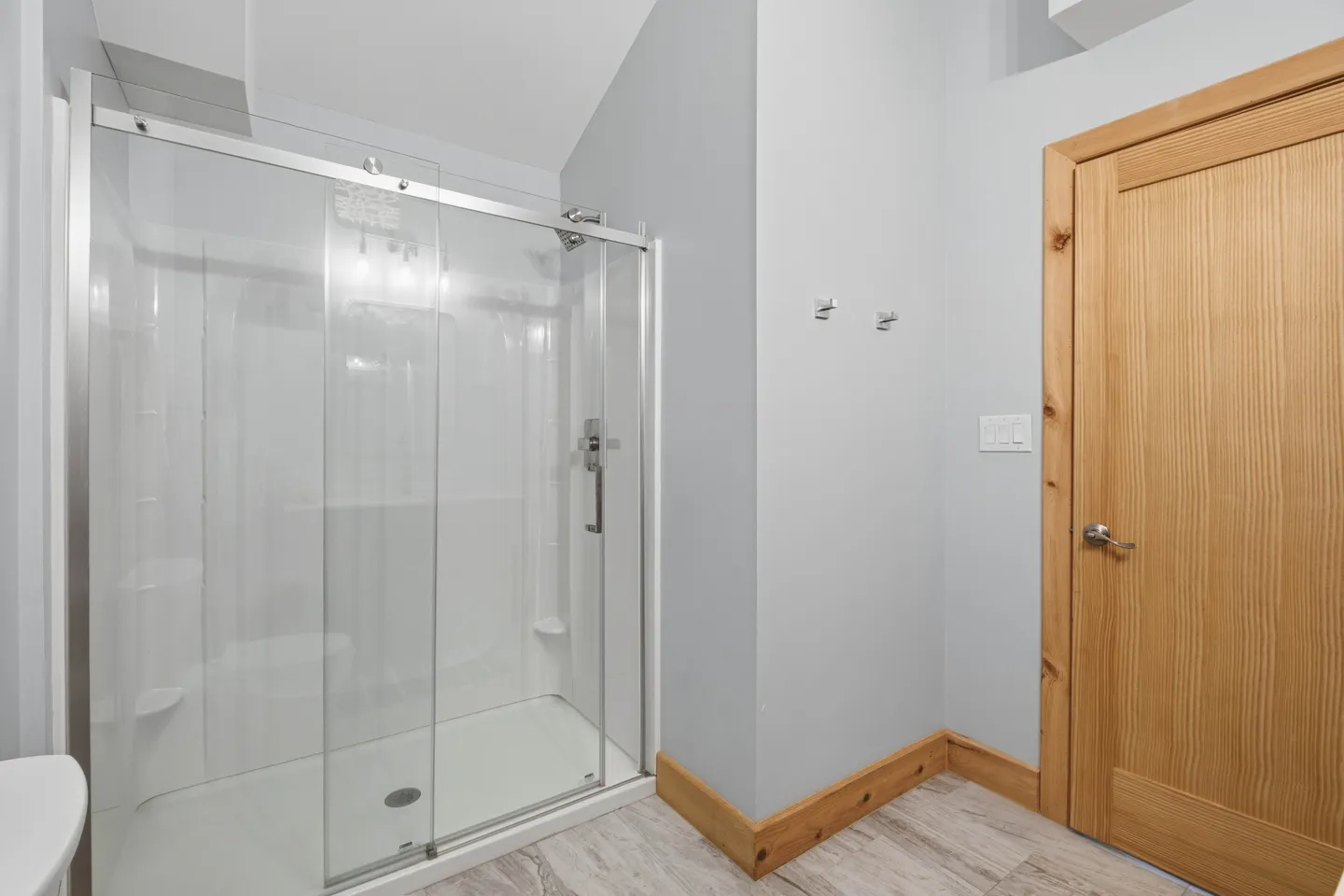 Bathroom with a glass-enclosed walk-in shower, wooden baseboards, and a natural wood door.