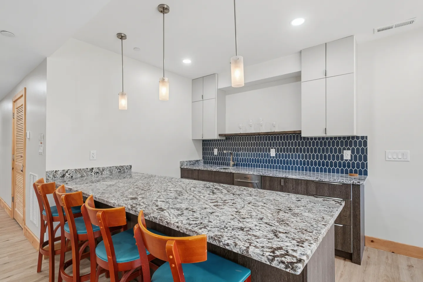 Wet bar area featuring a granite-topped peninsula with barstools, pendant lights, and blue geometric tile backsplash.
