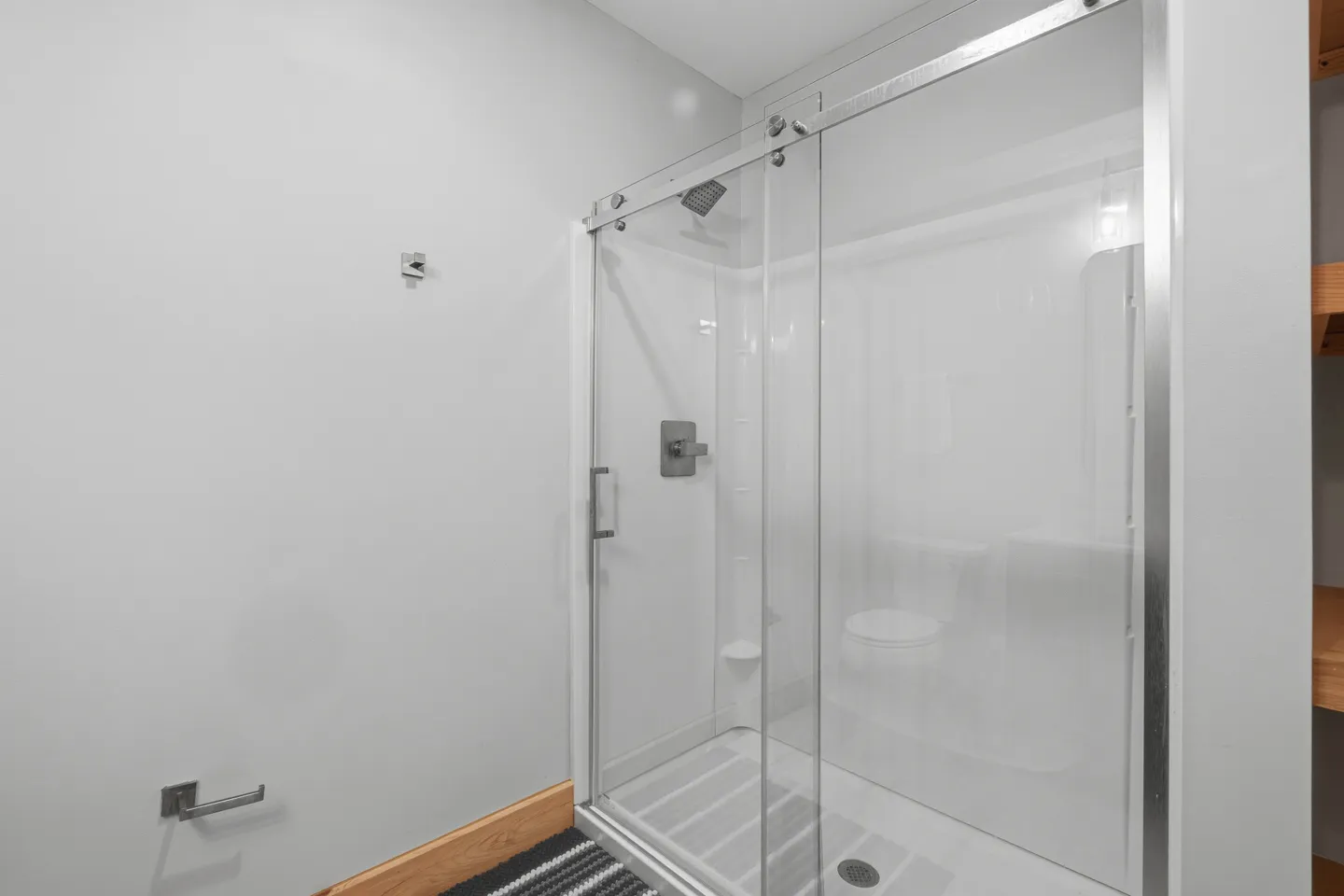 Bathroom with a sliding glass door shower stall next to a light-colored wall with a toilet paper holder.