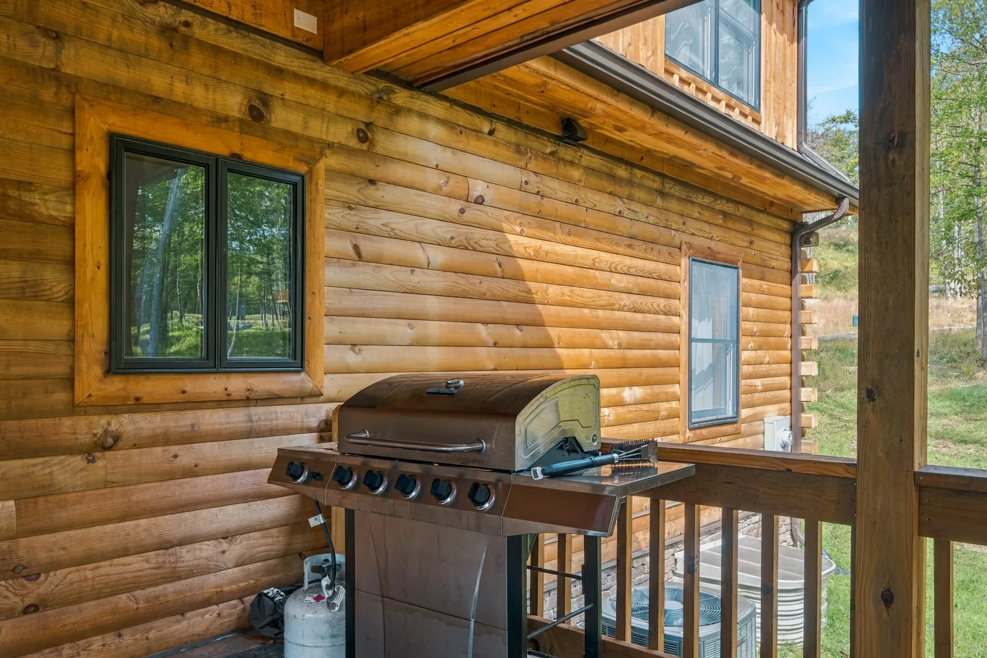 A stainless steel gas barbecue grill situated on a wooden covered porch next to the log cabin exterior.