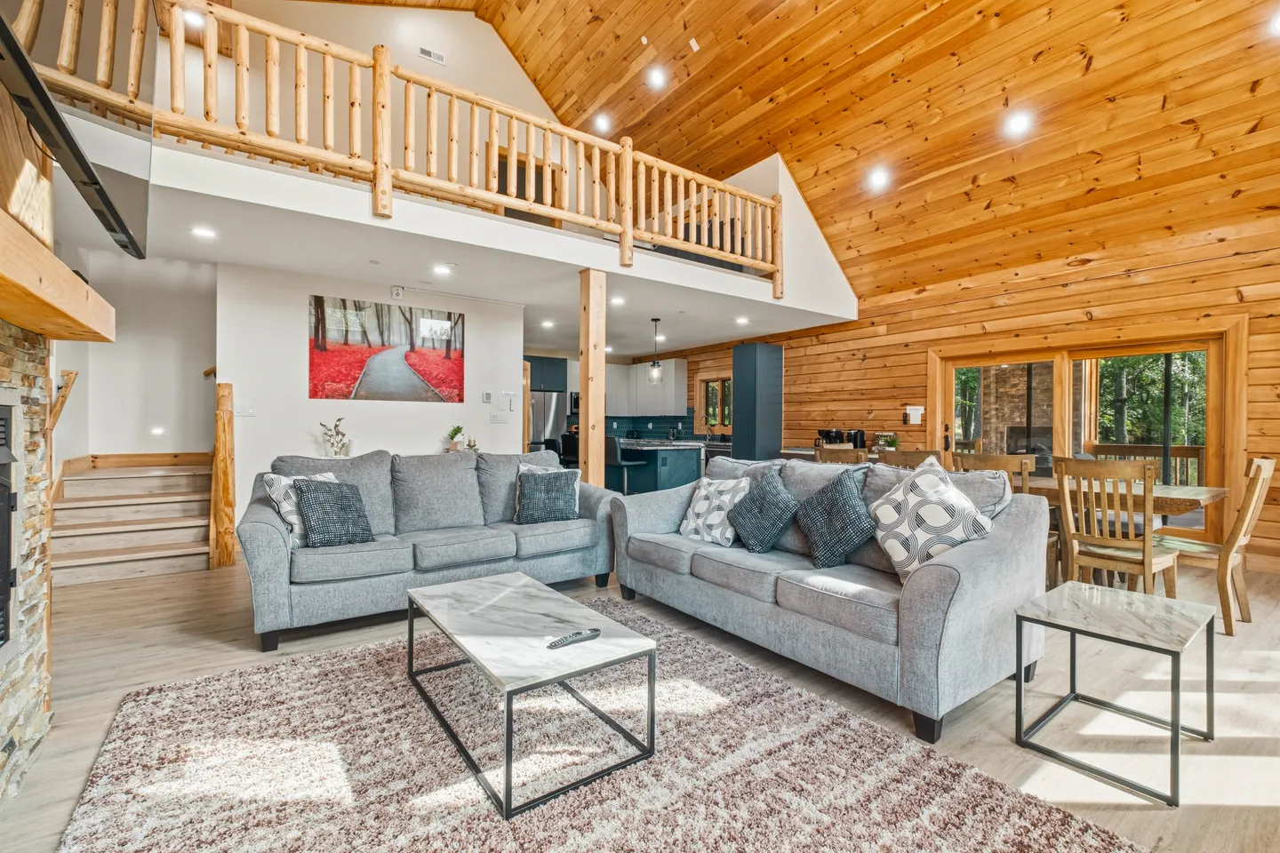 Open living area with two gray sofas, wood-paneled walls, an open loft above, and a dining table nearby.
