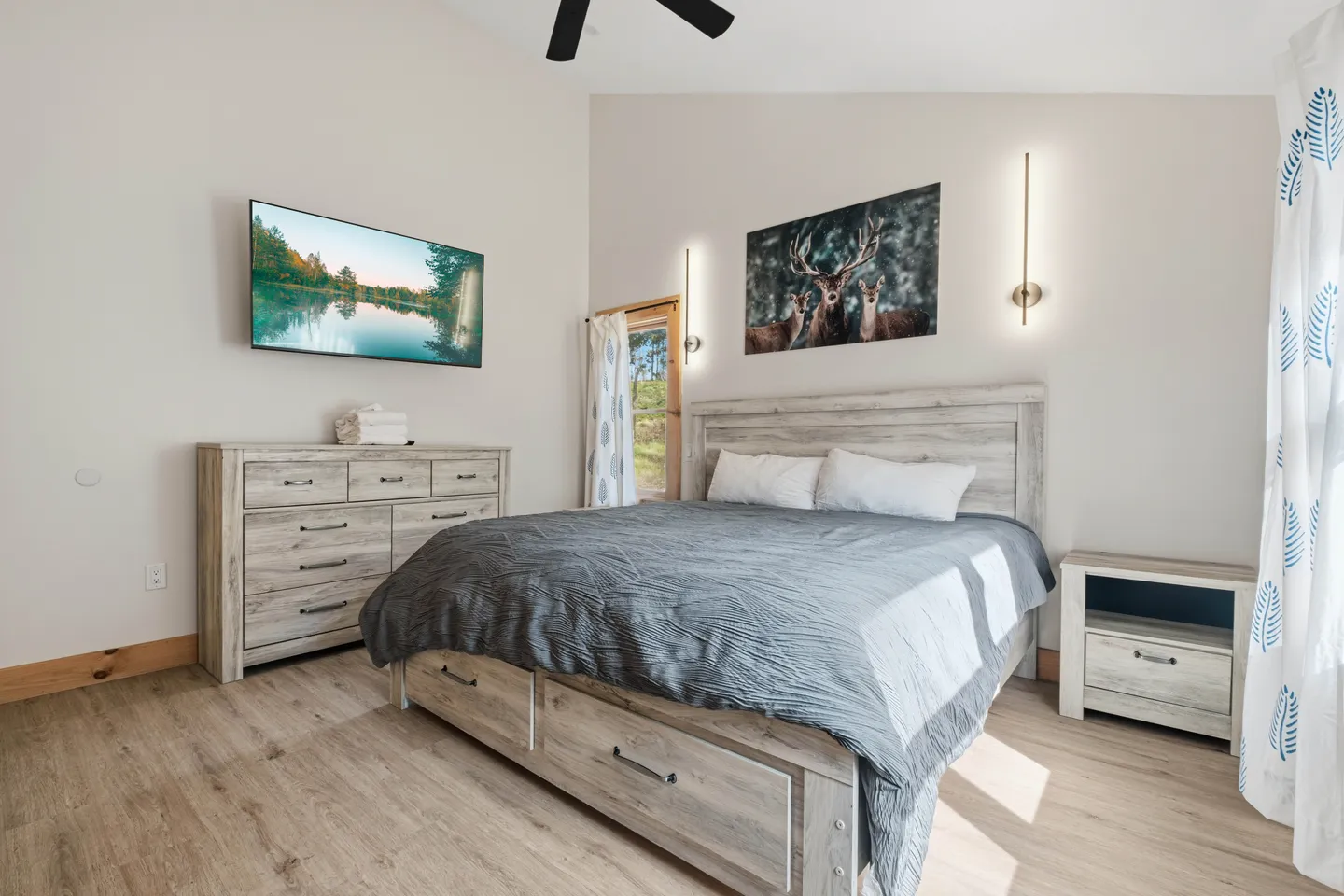 Bedroom with a bed with built-in storage drawers, matching nightstand and dresser, wall-mounted television, and deer artwork.