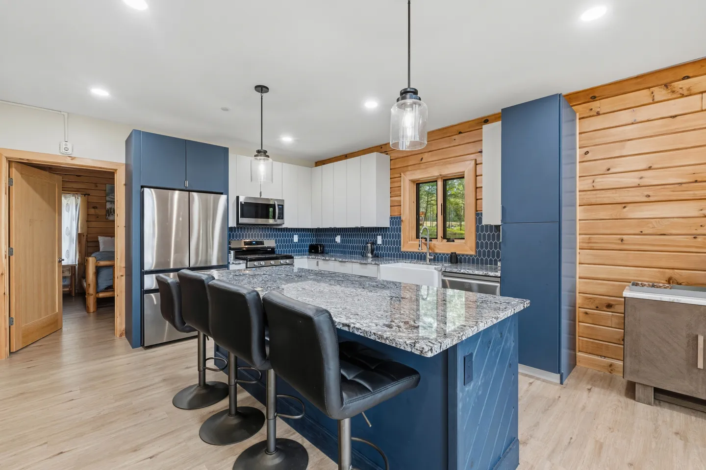 Kitchen featuring blue and white cabinetry, a granite-topped island with black barstools, and wood-paneled walls.