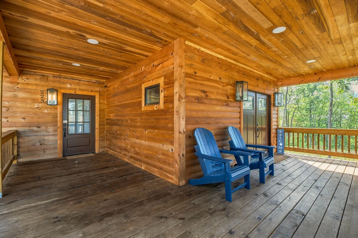 Covered wooden porch of a log cabin with two blue Adirondack chairs and an entrance door.