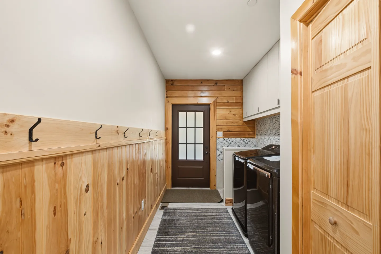 Mudroom and laundry area with wood wainscoting, coat hooks, dark washer and dryer, and an exterior door with glass panes.